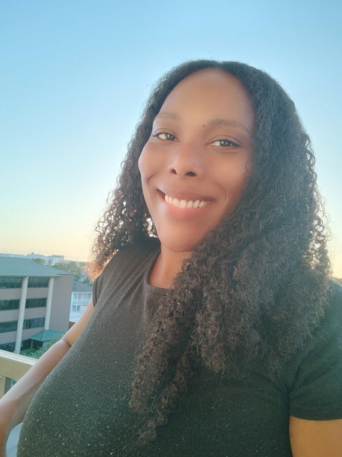 Woman wearing 22 inch kinky curly hair extensions in natural daylight on balcony showing texture, density and real-life movement